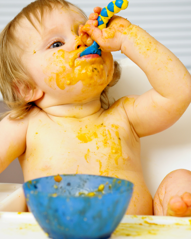 baby messily eating solid foods from a bowl