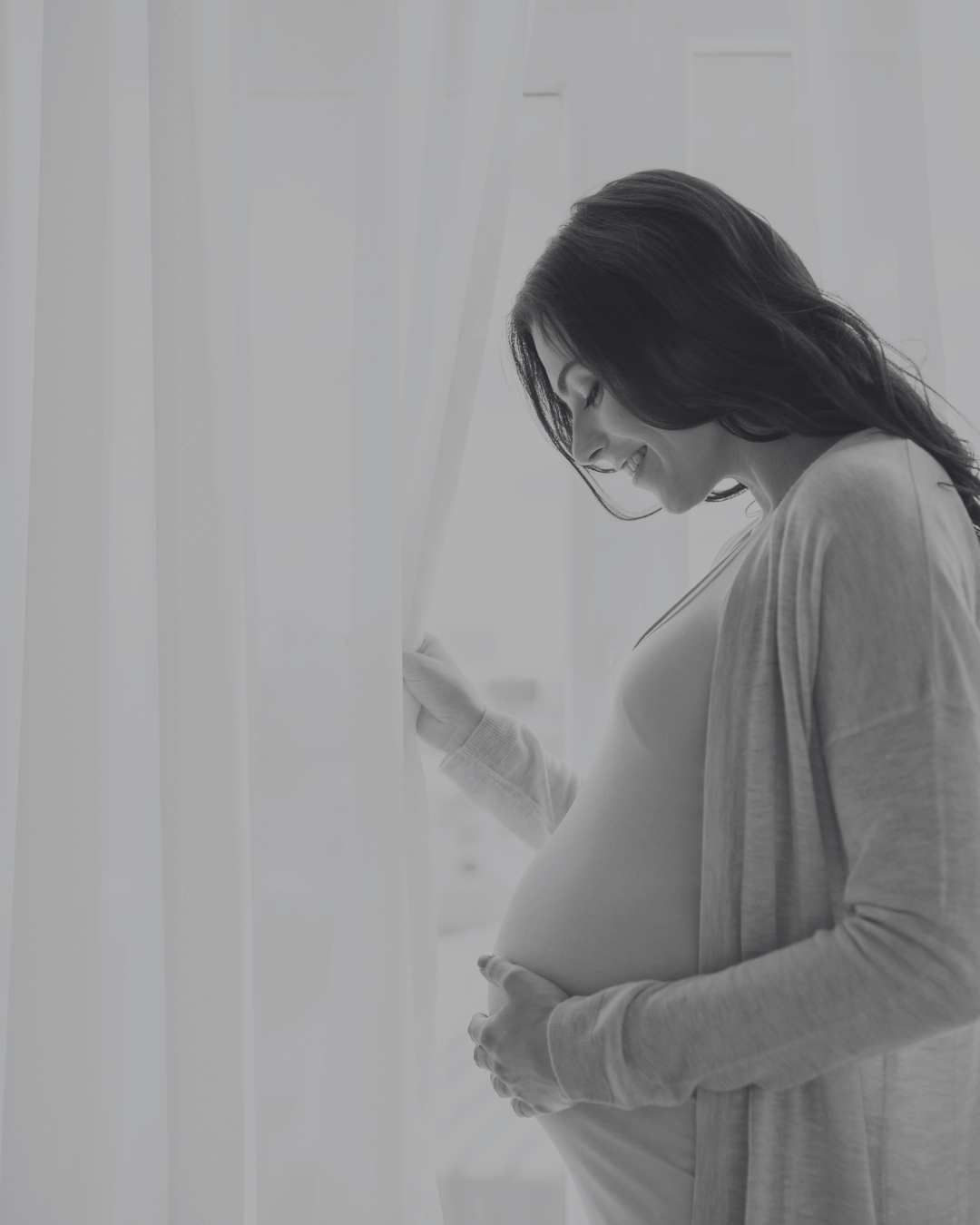 black & white portrait of smiling pregnant woman looking at belly